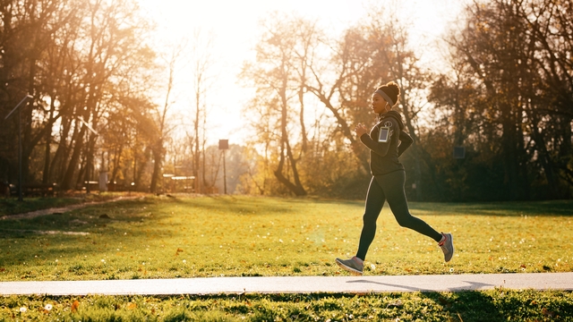 Woman wearing a grey jacket and headband running outside on a path in the woods